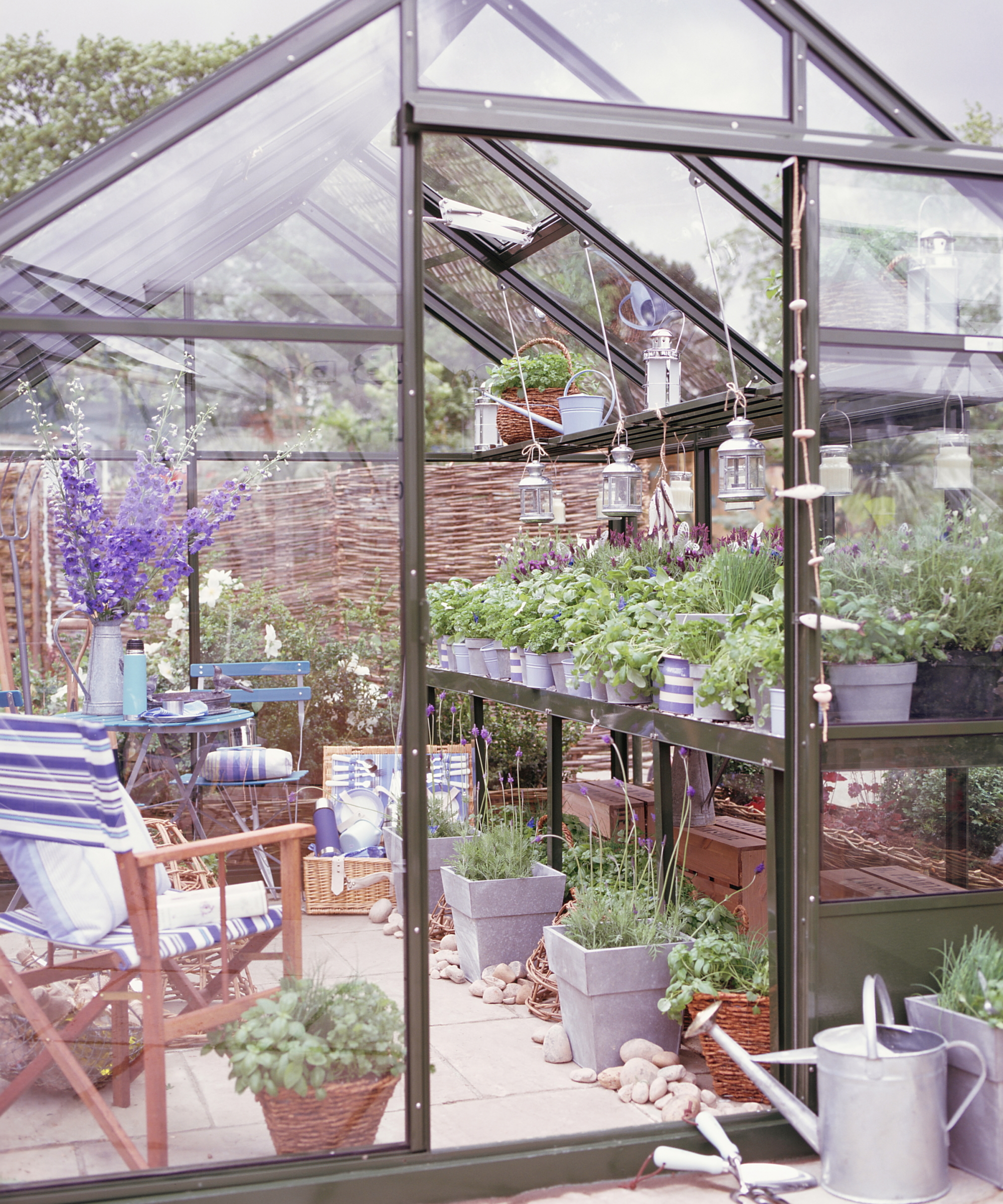 A greenhouse setup with propagation shelving covered in pots and seed trays, as well as a table and chairs