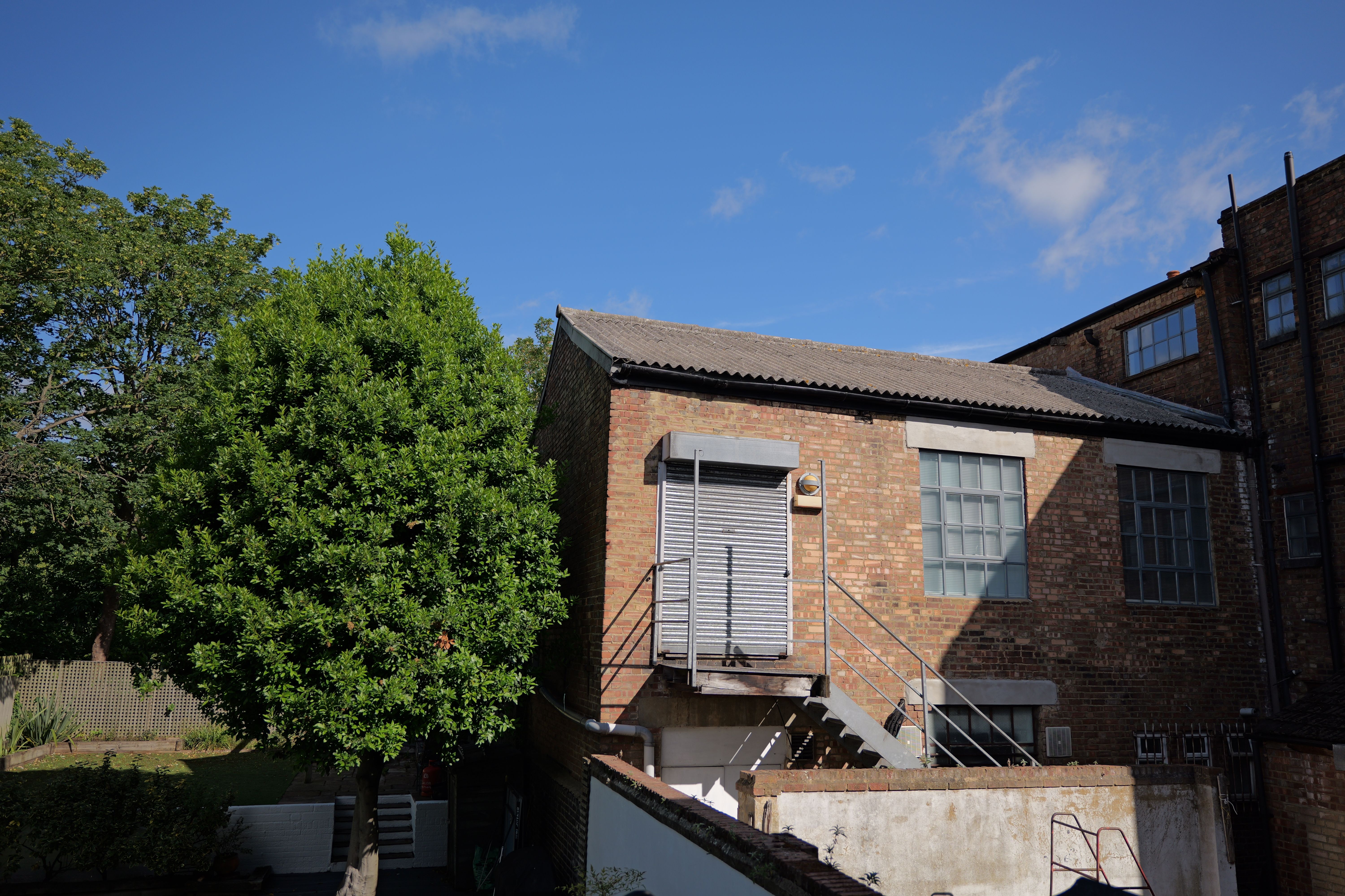 A warehouse next to a tree in front of a bright blue sky