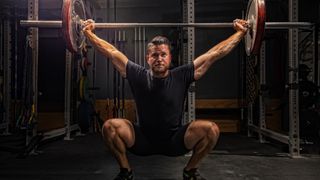 Man performing a snatch holding a barbell above his head in a squat