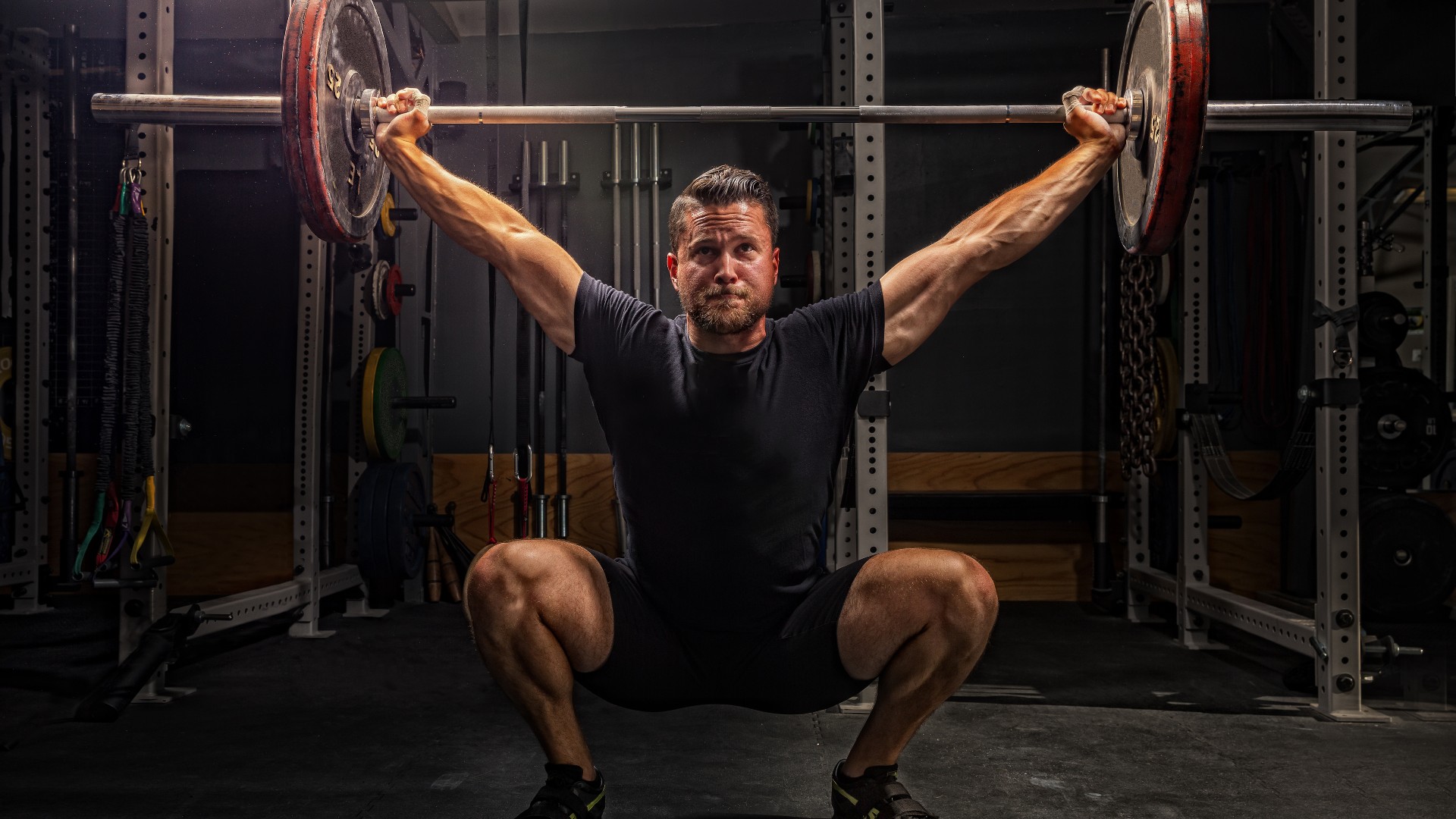 A man performs a snatch with a bar over his head in a squatting position