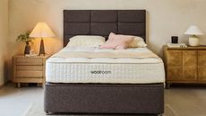 A Woolroom mattress on a gray bed frame against cream walls; a nightstand and a lamp either side of the bed.