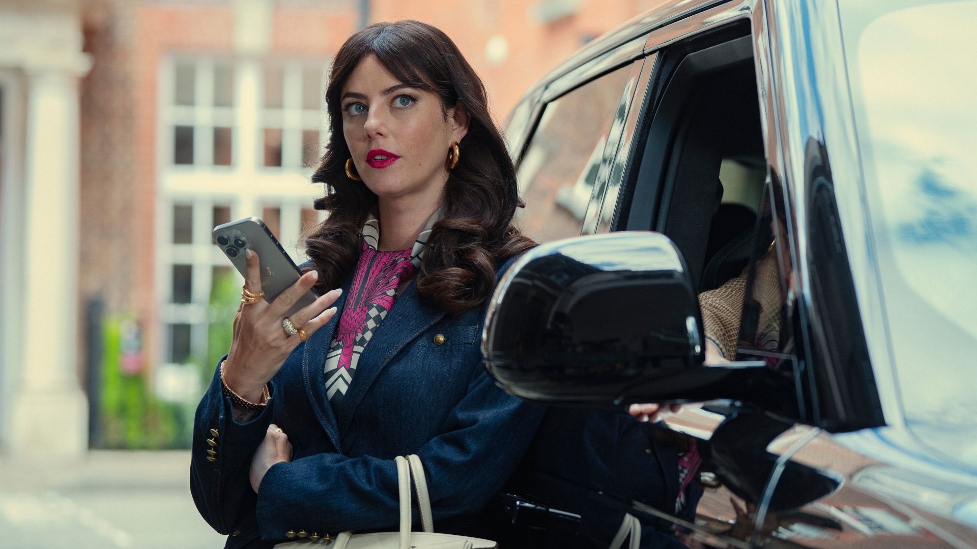 Susie leans against a Range Rover holding a phone