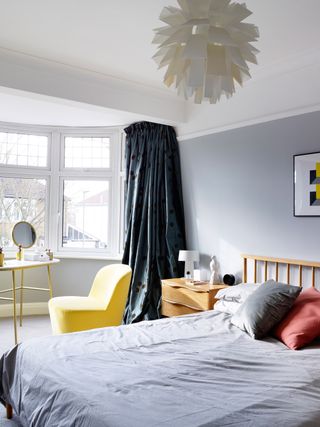 modern bedroom with grey walls, a statement pendant light, wooden bed and yellow chair