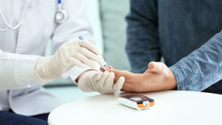 Gloved doctor pricks a patient's finger to conduct a blood sugar test