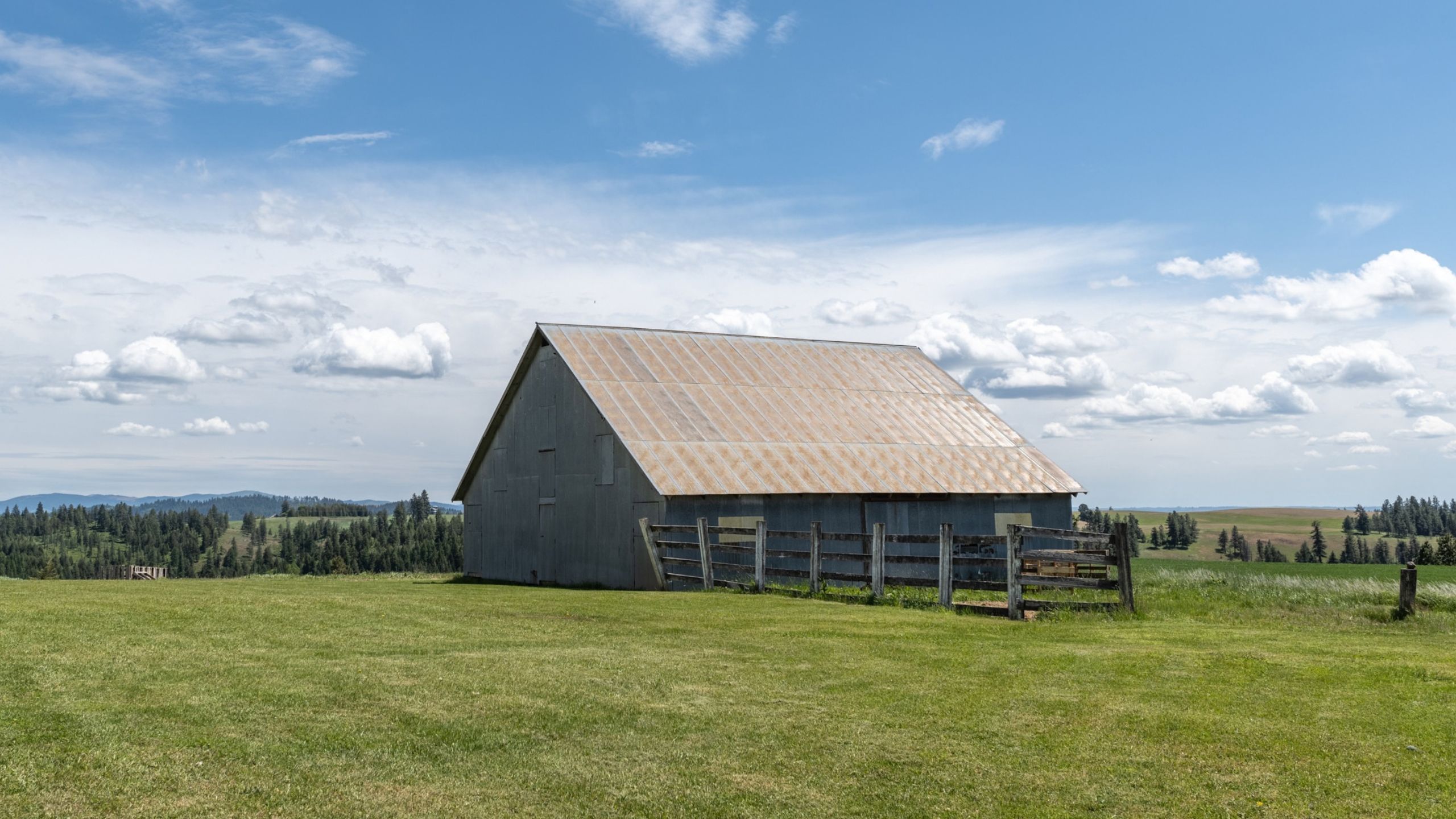 a rustic barn surrounded by lush farmlands, grass, distant mountains and trees