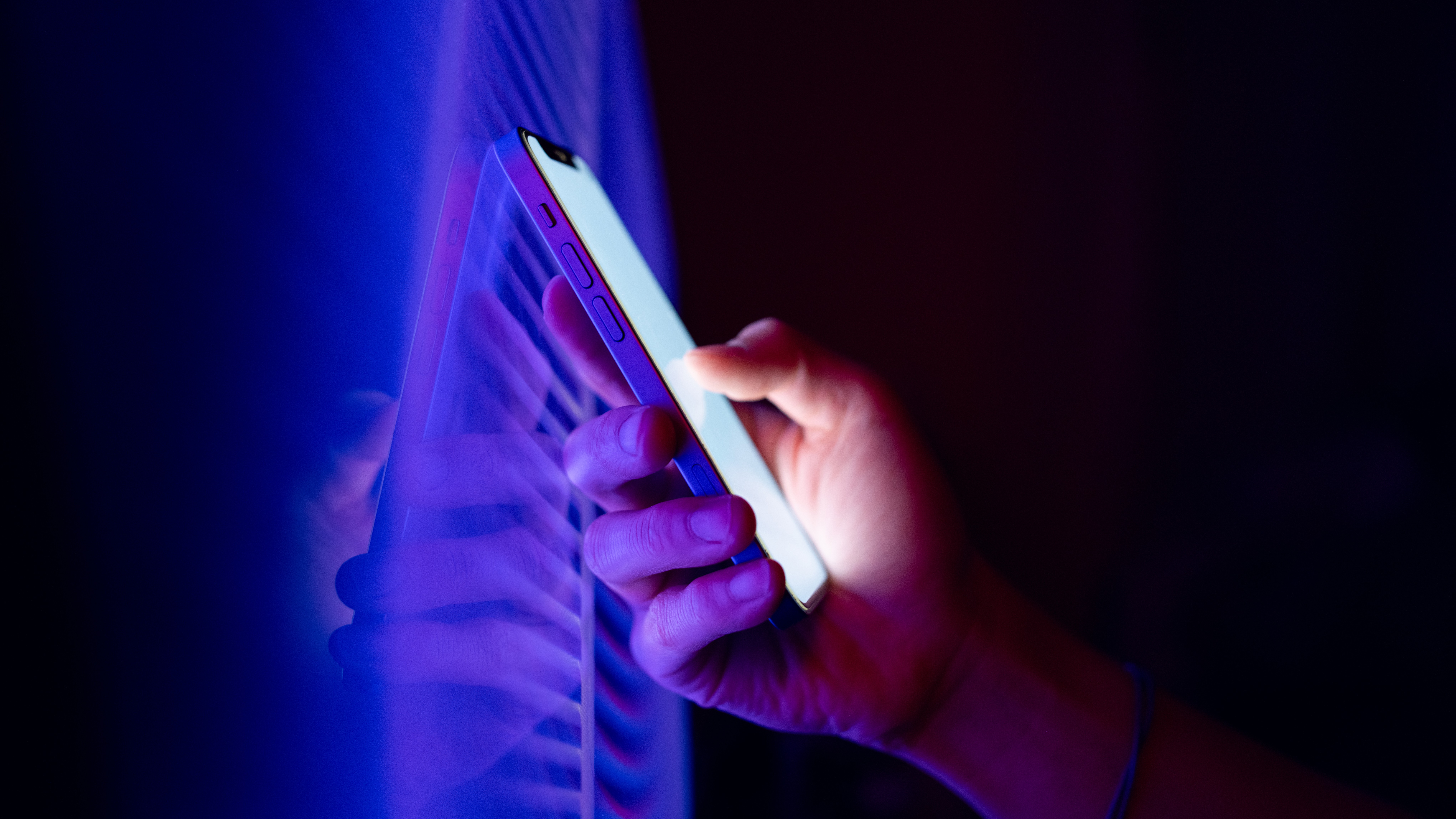 A conceptual photograph of a hand holding a phone in front of a blue LED display.