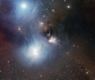 a telescopic view of wispy star-forming regions seen from afar. glowing stars puncture vast clouds of gas, scattered among stars