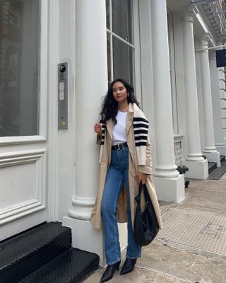 Kritsin wears blue jeans, trench coat, striped knit and black boots