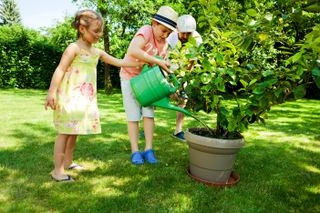 Father and two children watering potted plant in the garden