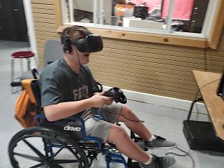 Boy in wheelchair smiles while using VR/AR headset and controller.