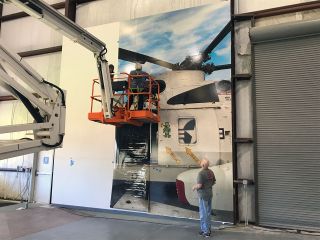 A photo realistic mural of Helo 66, a Sikorsky Sea King helicopter used to recover the Apollo crews after their splashdowns, serves as the backdrop for the Apollo 13 statue inside the Saturn V Building at Space Center Houston.
