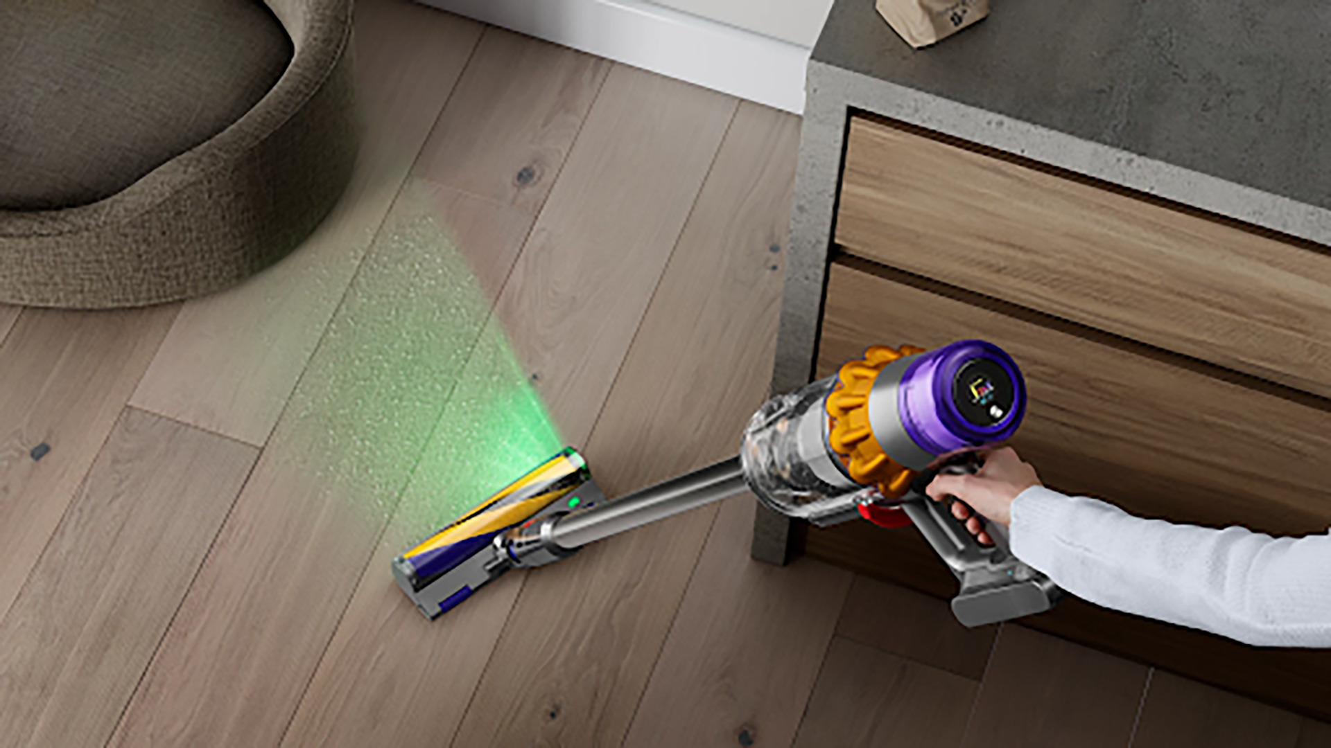 Dyson stick cordless vacuum used on wood floors with a green light.