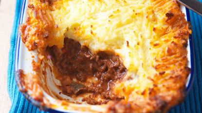 Cottage pie in oven tin with one large scoop taken out showing the meaty filling