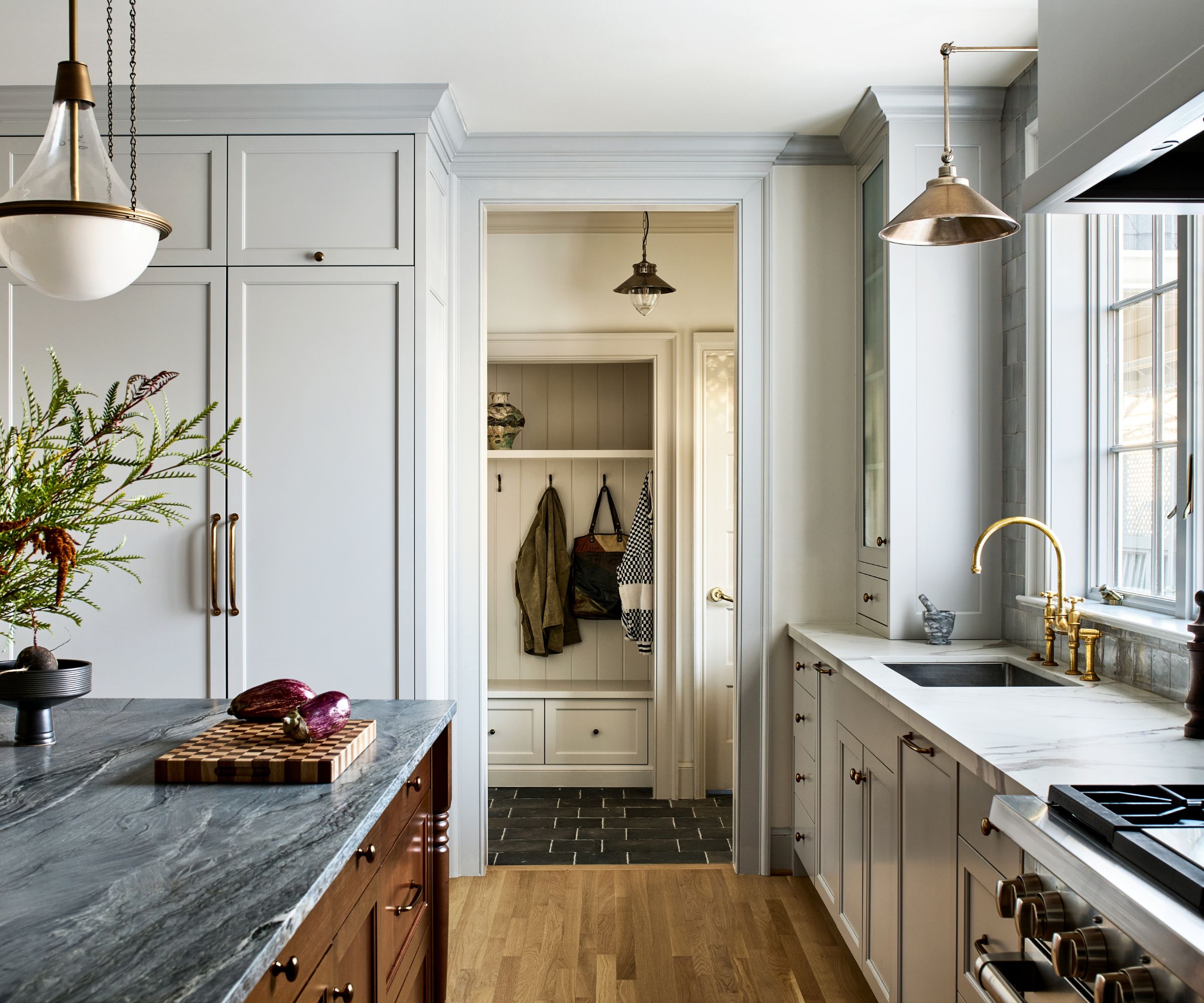 A transitional kitchen with pale blue cabinets and walls, a white ceiling, and wooden flooring. A dark wood kitchen island with a dark gray marble countertop and a white and brass pendant light.