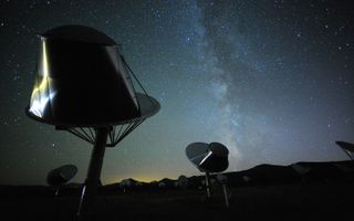 radio telescopes point up at the dark night sky with mountains in the background