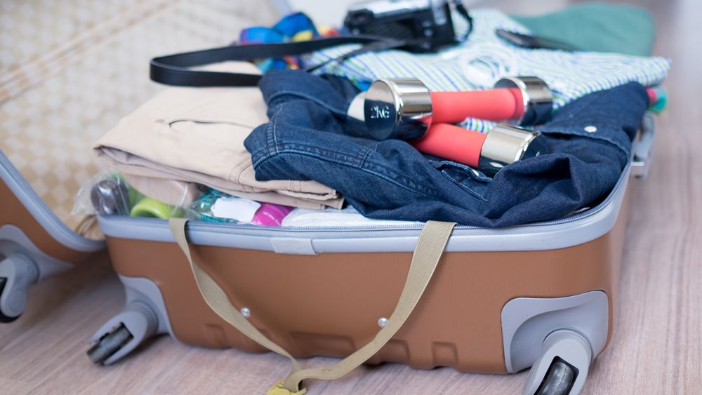 Suitcase with dumbbells on top of holiday clothes