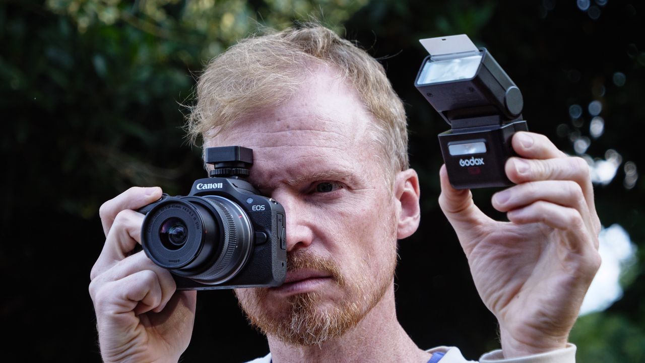 Photographer and TechRadar's Cameras Editor Tim Coleman holding a Canon camera up to his eye, there's a Godox iT32 camera flash alongside to the camera