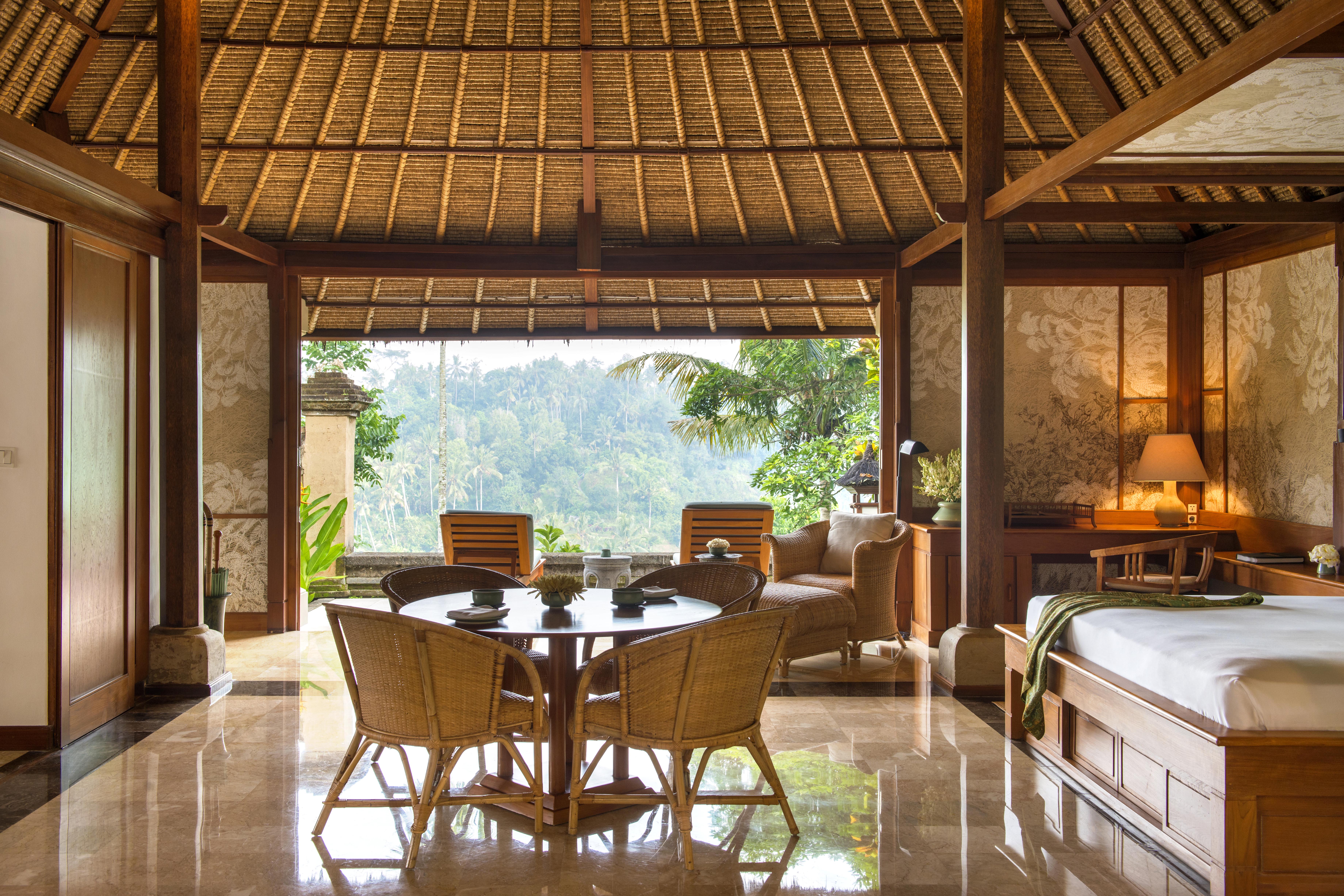 Balinese-style hotel room with a bed, round table and rattan chairs, floral wallpaper and a pitched roof