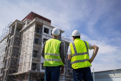 Engineers in hard hats inspect a large building covered in scaffolding.
