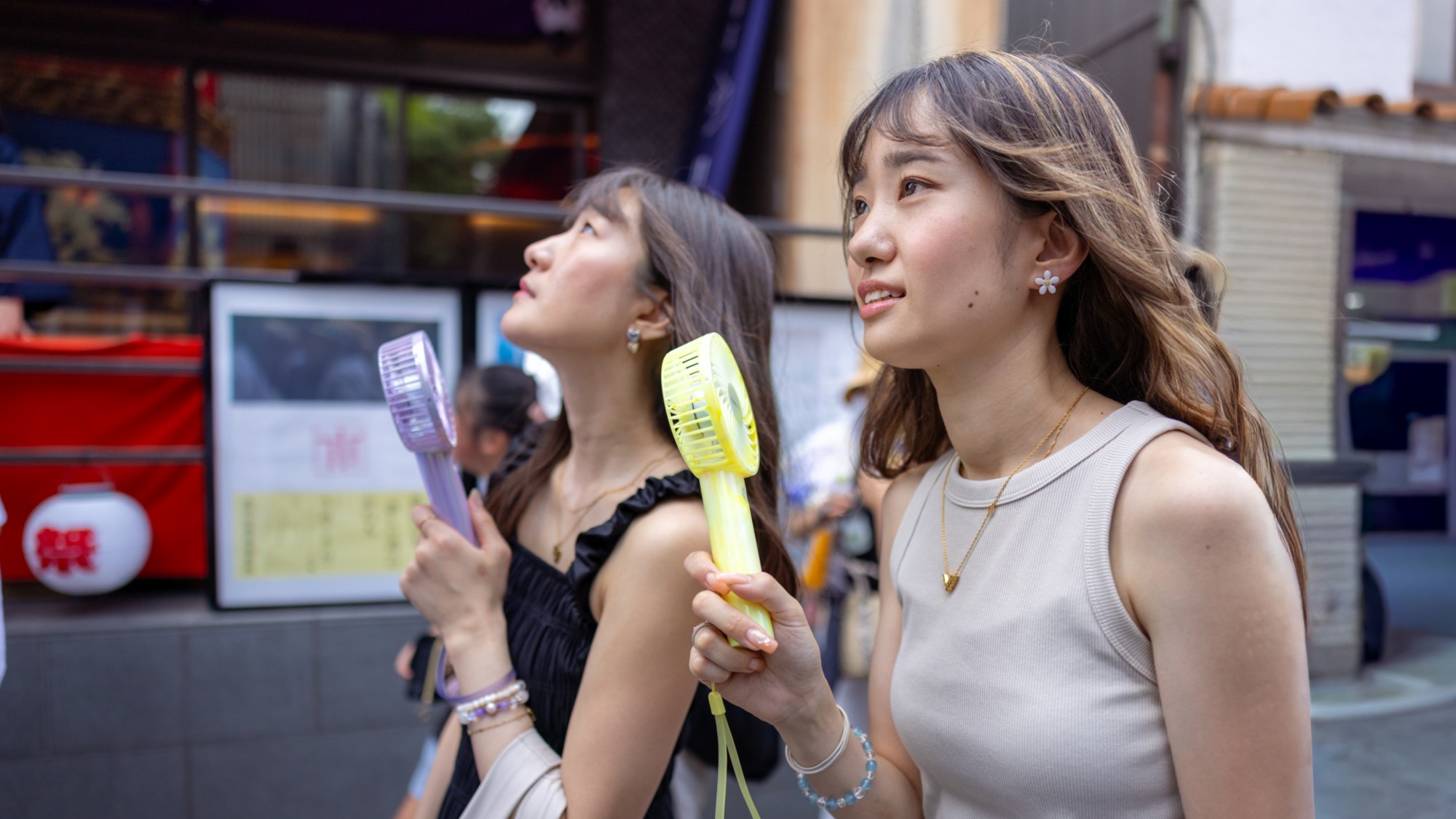 Two young Japanese women walking down a street while using hand fans