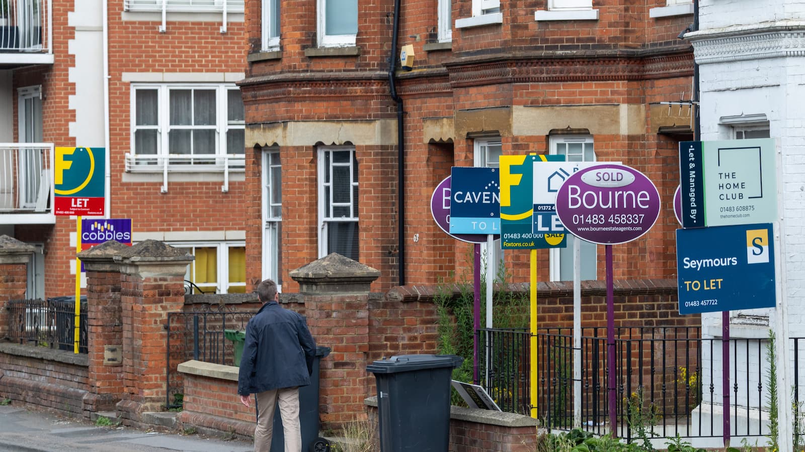 A man walking along a street of house that are for sale