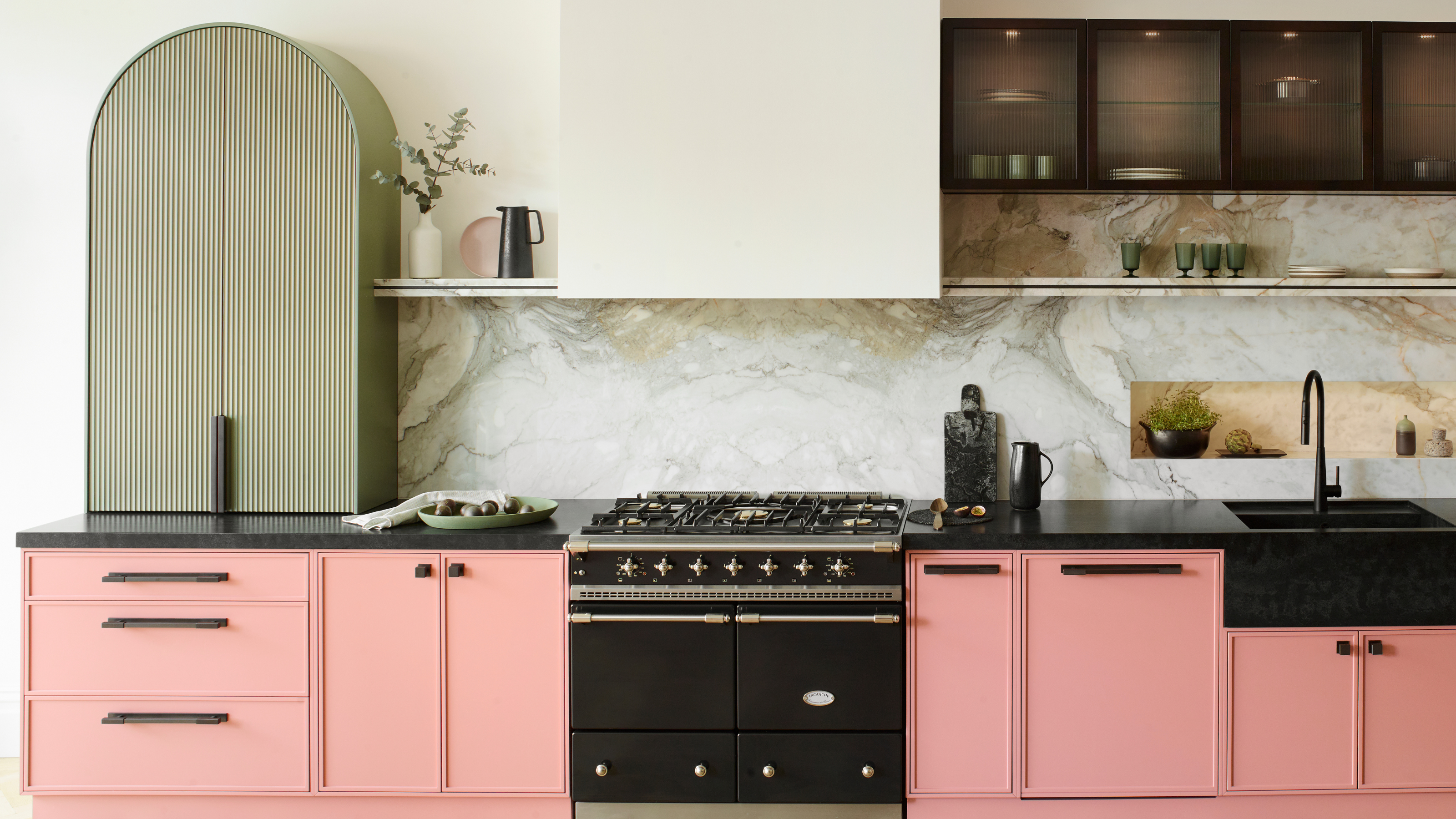 A modern one-wall kitchen with pink and black cabinetry and one tall cureved green unit with a fluted front