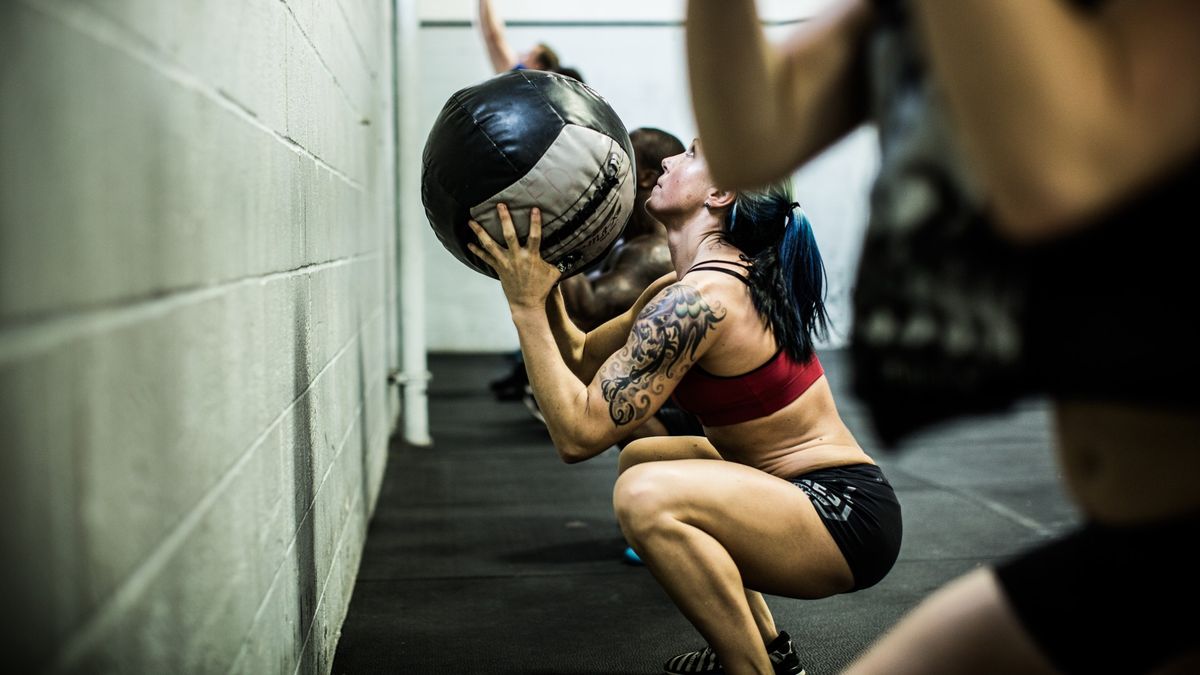 Woman in a squat position throwing a weighted ball towards a wall during workout
