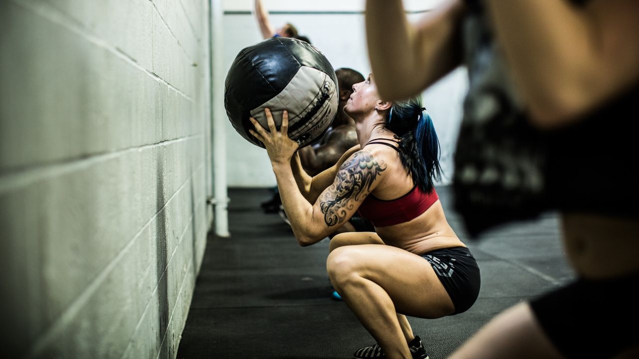 Woman in a squat position throwing a weighted ball towards a wall during workout