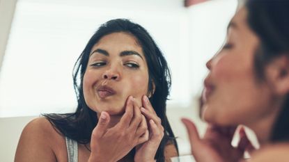 Shot of a young woman squeezing a pimple on her face at home