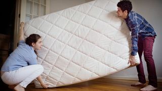 A man and woman lifting each side of a mattress to rotate it