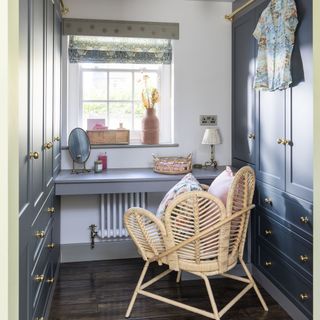 Dressing room with blue built in wardrobes on both sides with rattan chair and desk area.