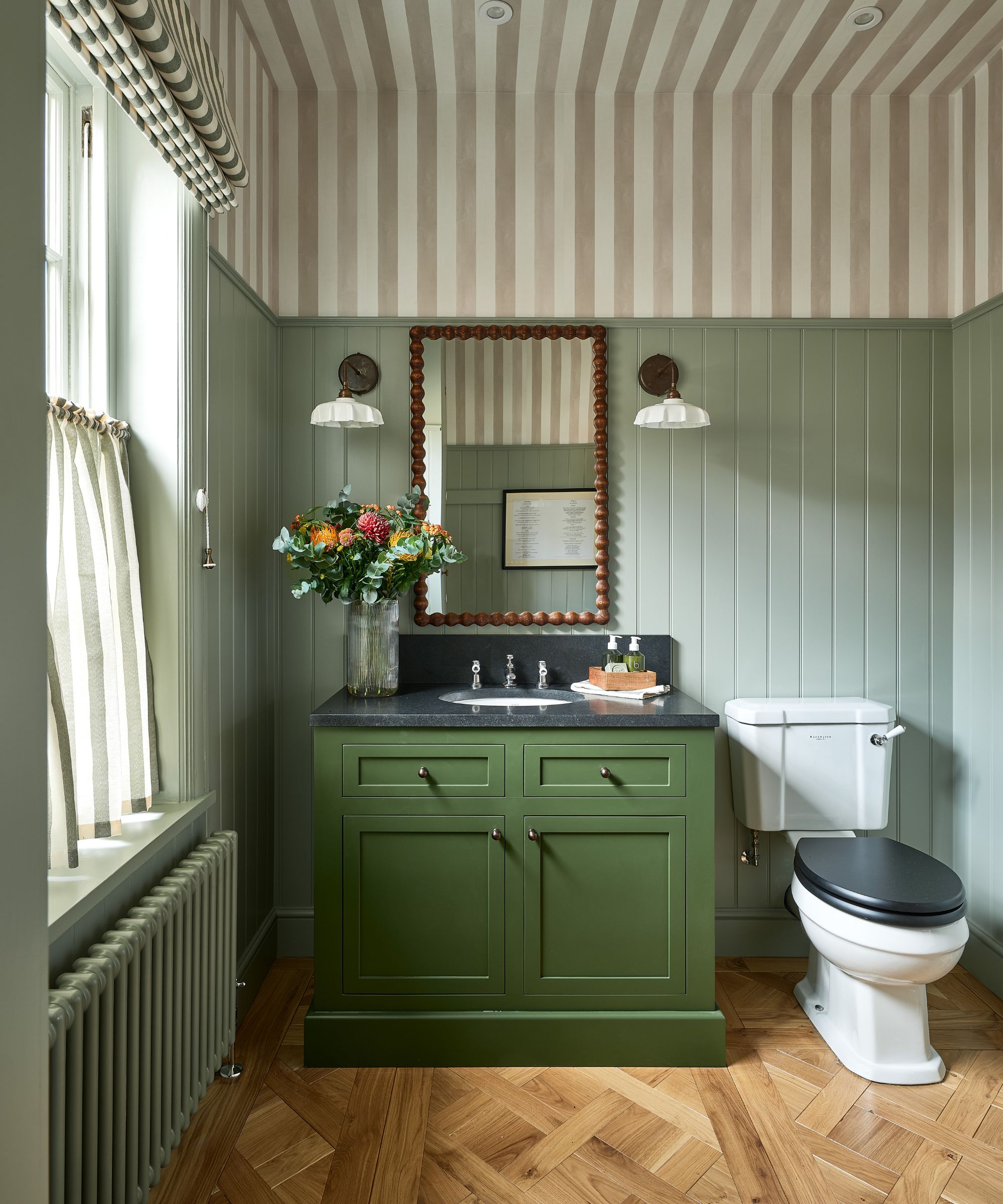 A powder room decorated with sage green wall paneling and striped wallpaper on the ceiling