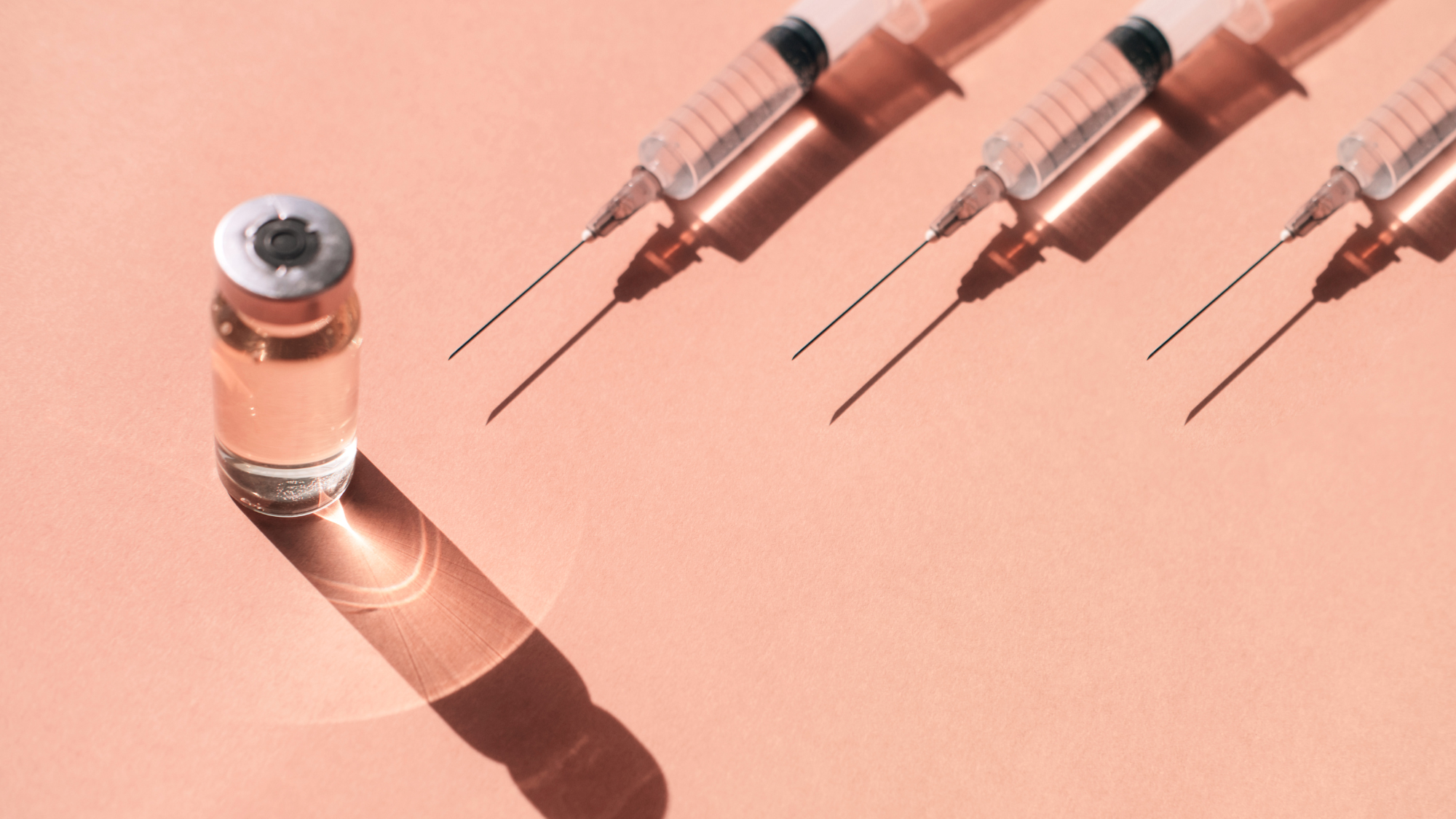 Pattern made with many plastic disposable sterile syringe and sealed vial of liquid remedy placed on pastel peach orange background with shadows and light reflections