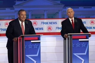 two men in suits laugh on a stage behind lecterns during a debate