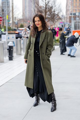 Katie Holmes wearing an olive green coat, a black turtleneck, a black skirt, and black heels