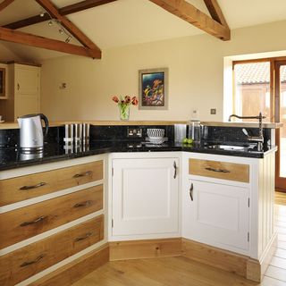 kitchen area with white wall and wooden floor and wooden cabinets with black worktop