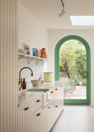 A kitchen with paneled cabinets and a white worktop. The door leading to the garden has a green framing