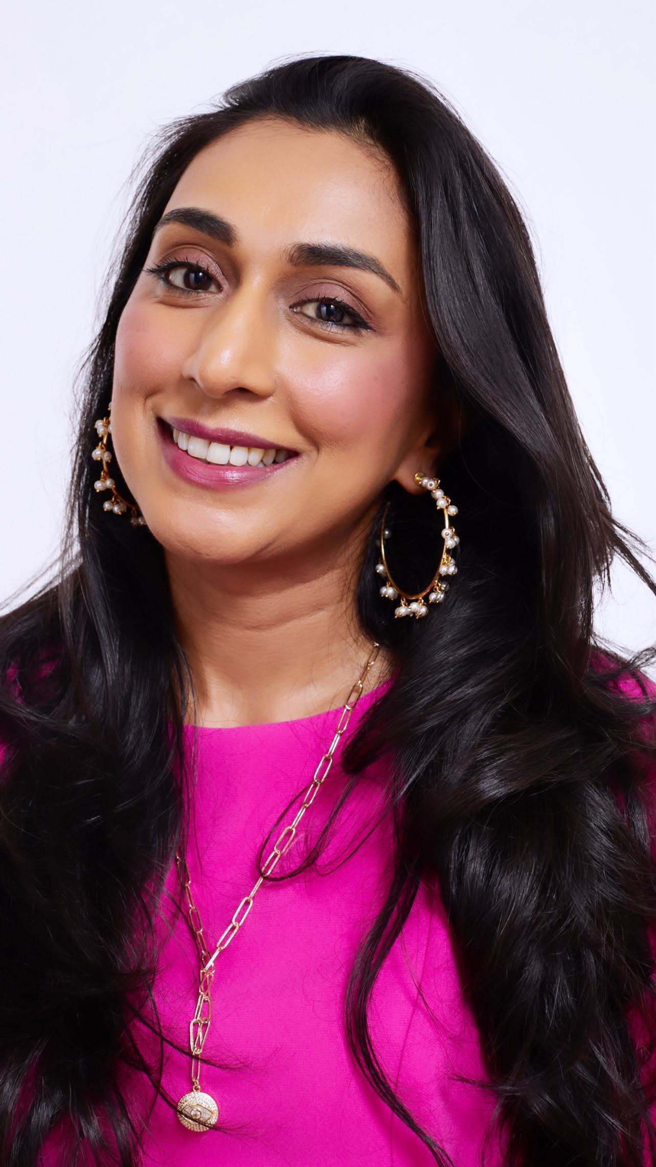 A headshot of a woman with dark hair wearing a pink top smiling at the camera