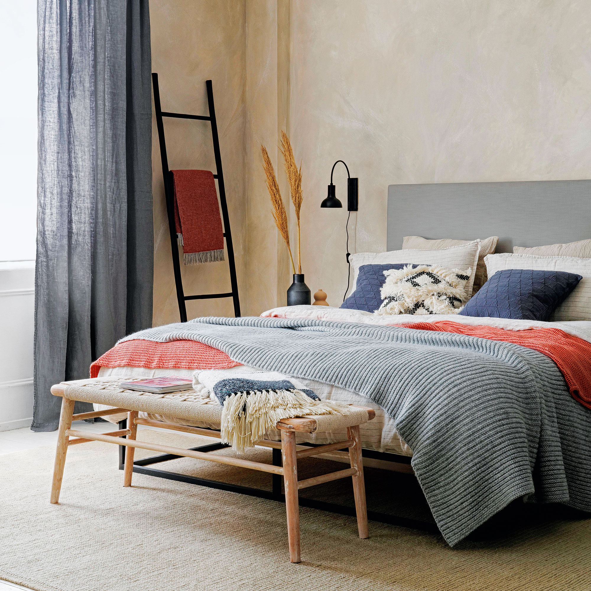 Neutral bedroom with grey upholstered double bed dressed in layered linens including a grey knitted throw
