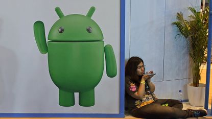 Woman using a phone sat next to an Android poster
