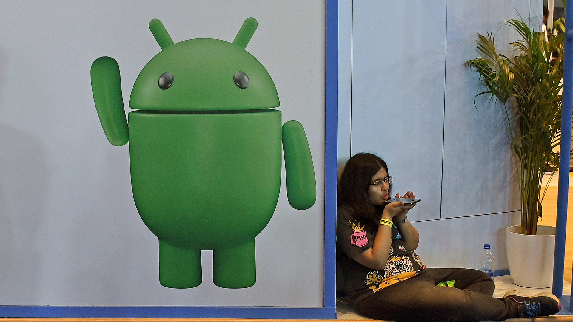 Woman using a phone sat next to an Android poster