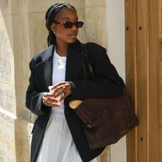 Woman wears black blazer, white t-shirt, white skirt and brown handbag