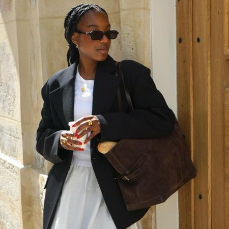 Woman wears black blazer, white t-shirt, white skirt and brown handbag