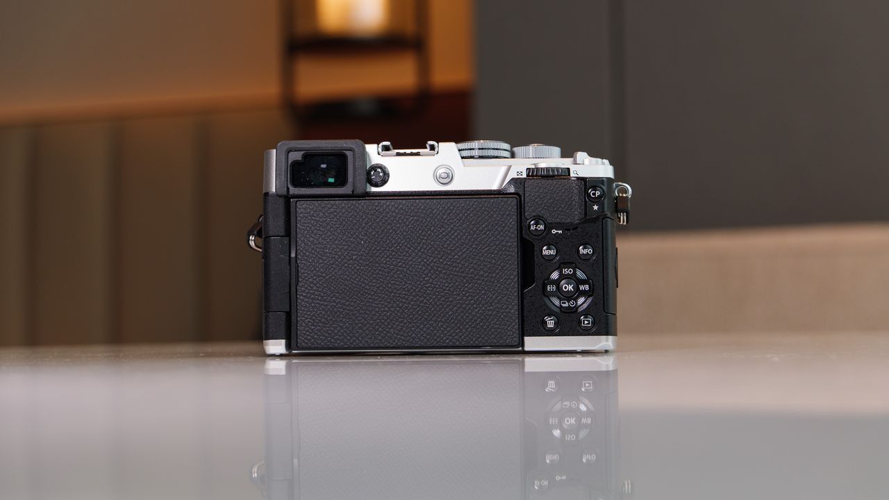 Rear view of the OM System PEN mirrorless camera, on a white marble surface in a modern room with lantern in the background