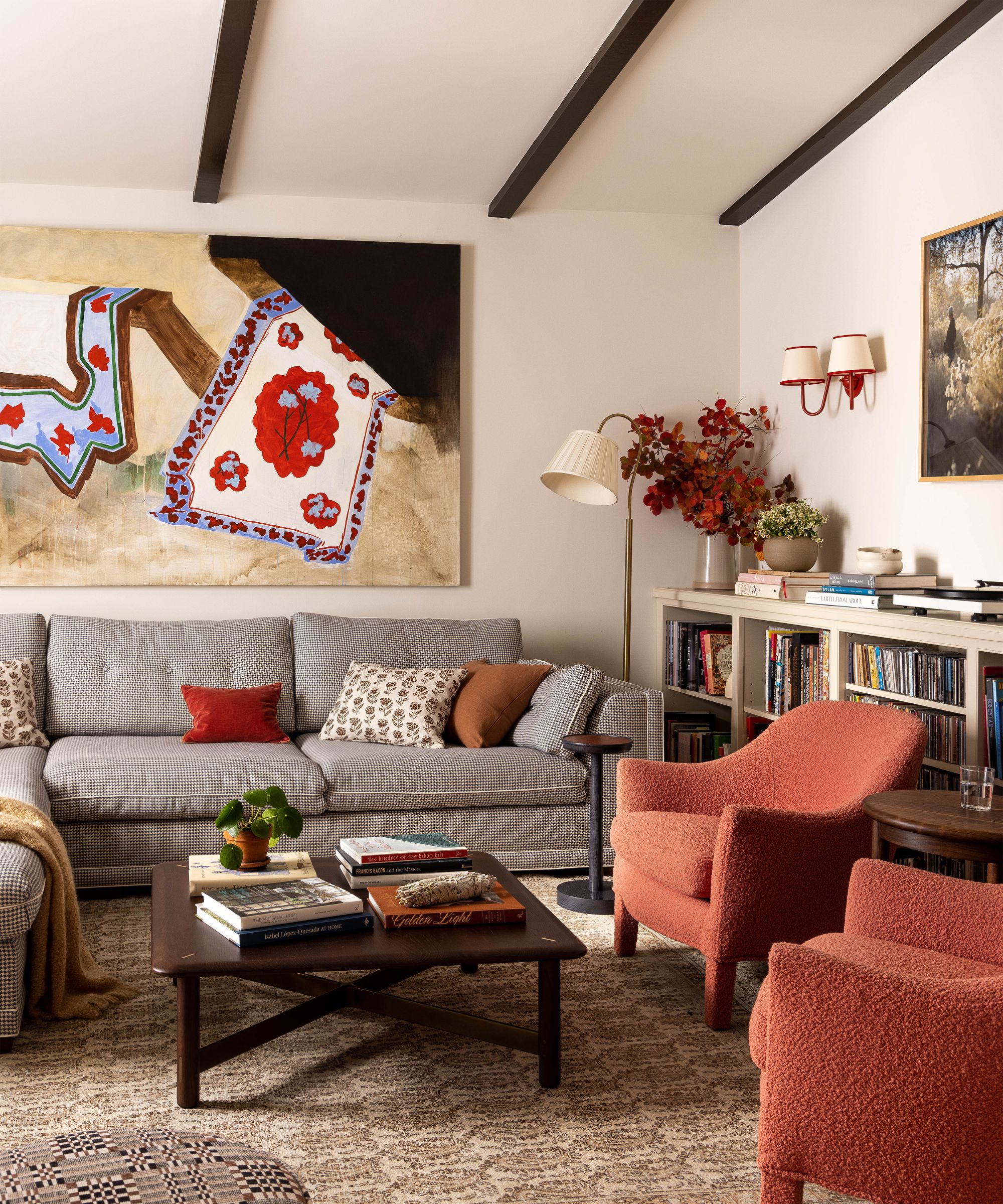 traditional cozy living room with pale pink walls, wooden ceiling beams, gray sofa, and brick red armchairs