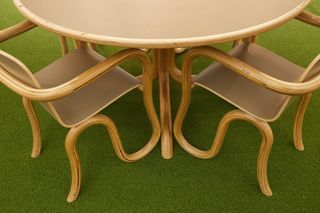 Close up view of a wooden and beige table and chairs with curved legs on green flooring in the Netjets VIP Lounge at Art Basel