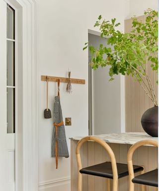 A white wall with a rack storing kitchen utensils and an apron