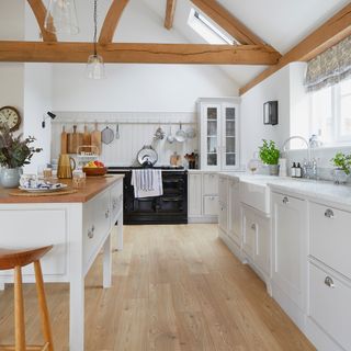 country kitchen with wood beams on ceiling, a freestanding island, and laminate light-wood floors