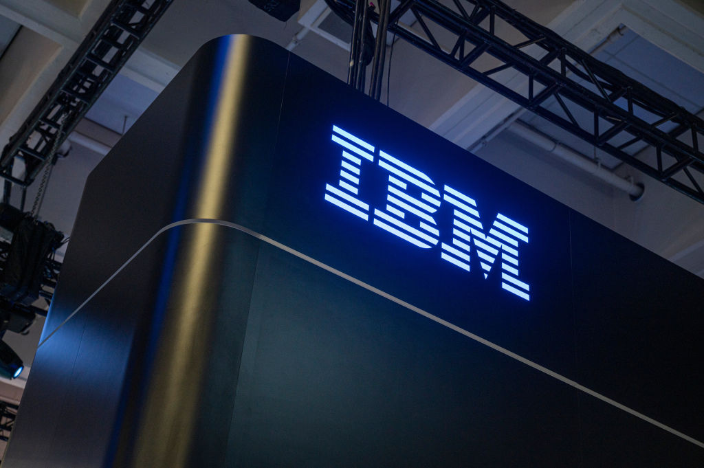 Close-up photo of the side of a dark blue conference booth with a glowing neon IBM sign on the side