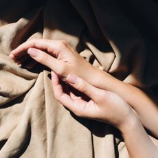 Two hands on beige sheet wearing glittering gel nail polish